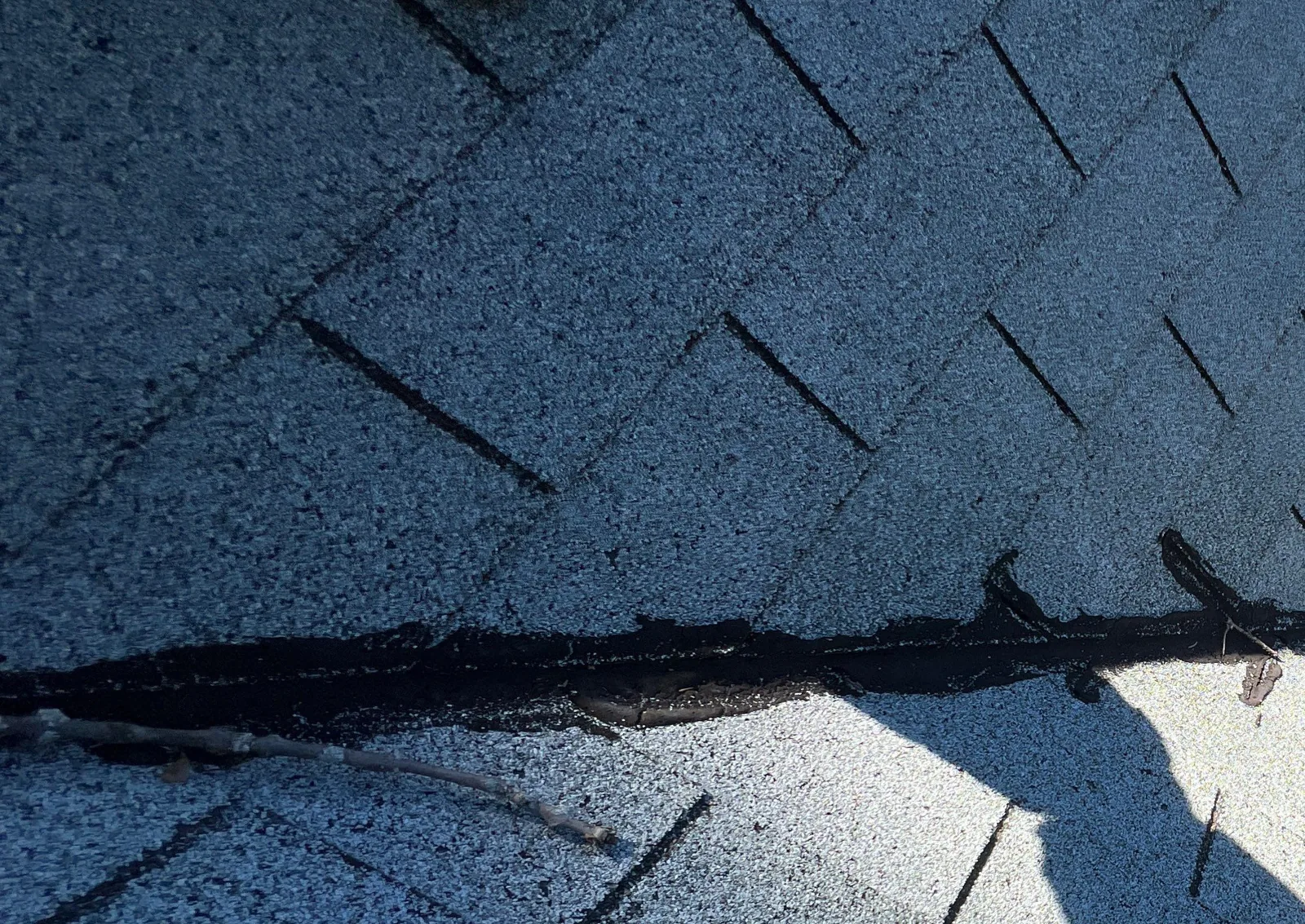 Separated shingle seam along a roof hip after storm wind lifted the shingles