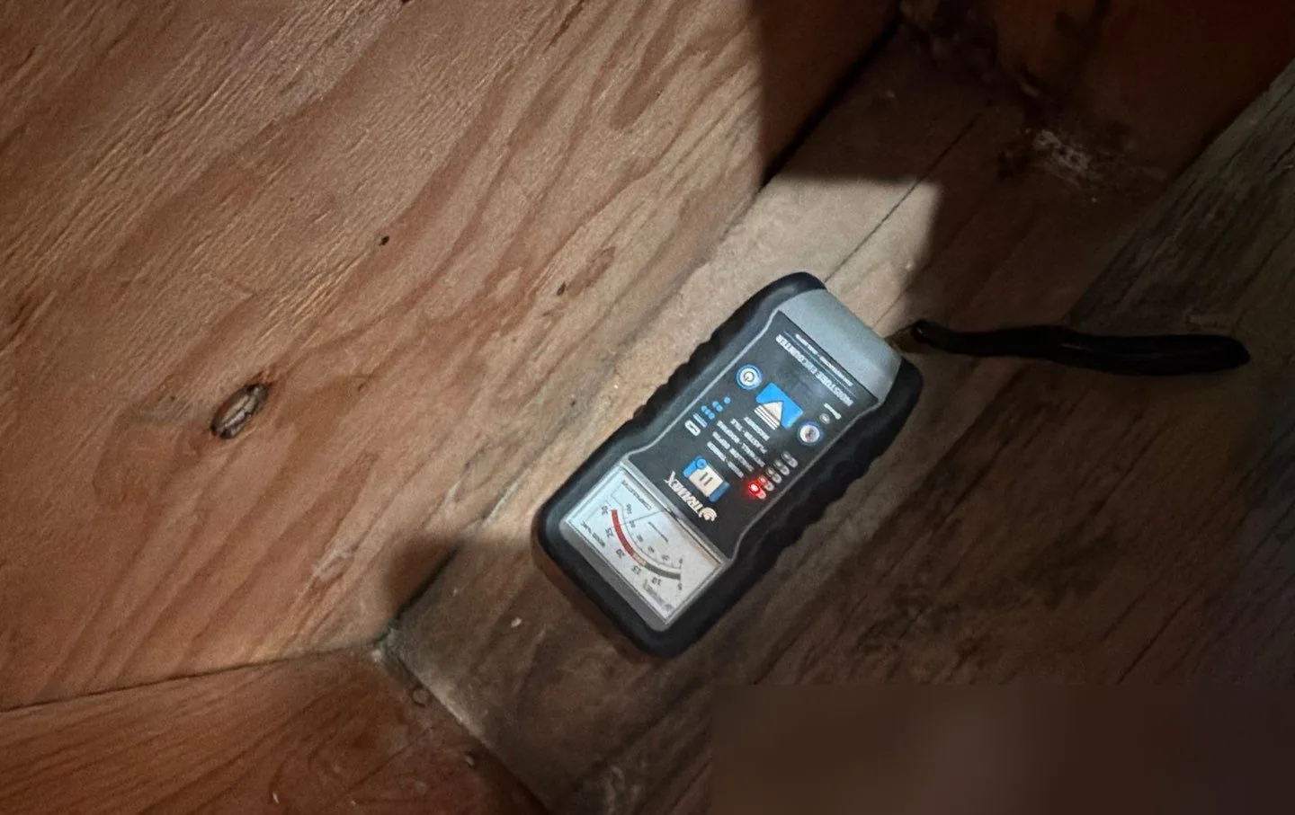 Pin-type moisture meter resting on a wood subfloor and joist during a mold inspection in a New Jersey home