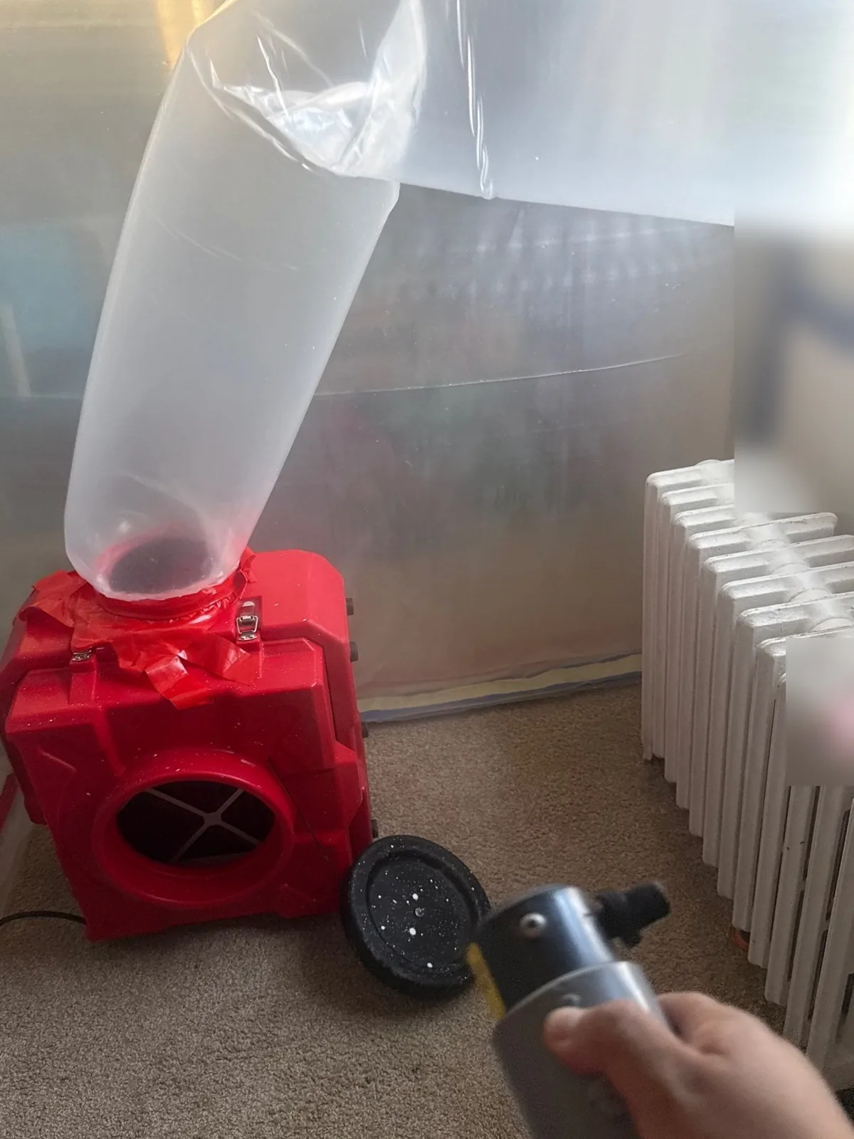 Air scrubber with a ducted hose inside a plastic containment barrier in a water-damaged room