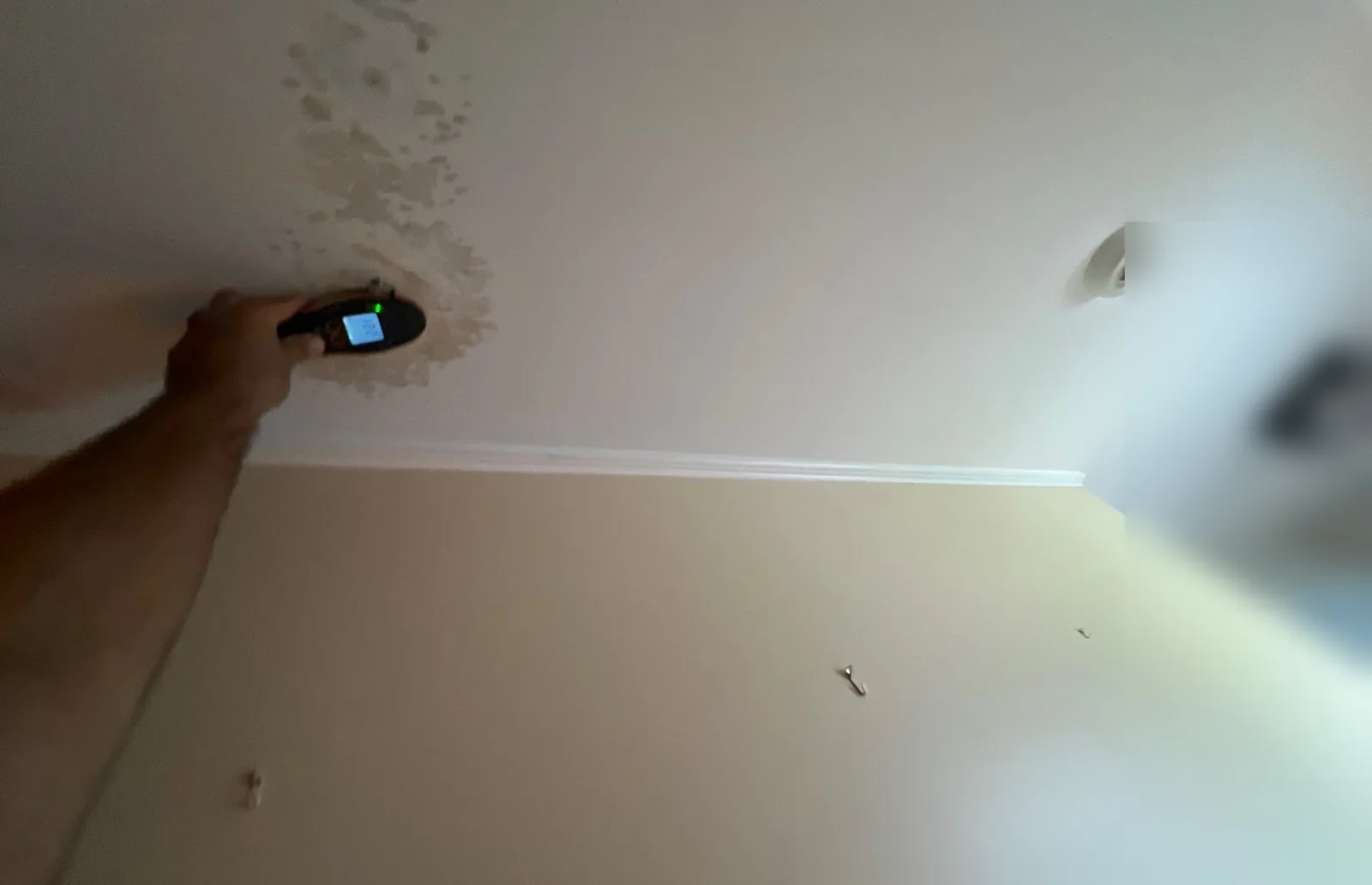 Technician holding a moisture meter against a water-stained ceiling after a leak from above