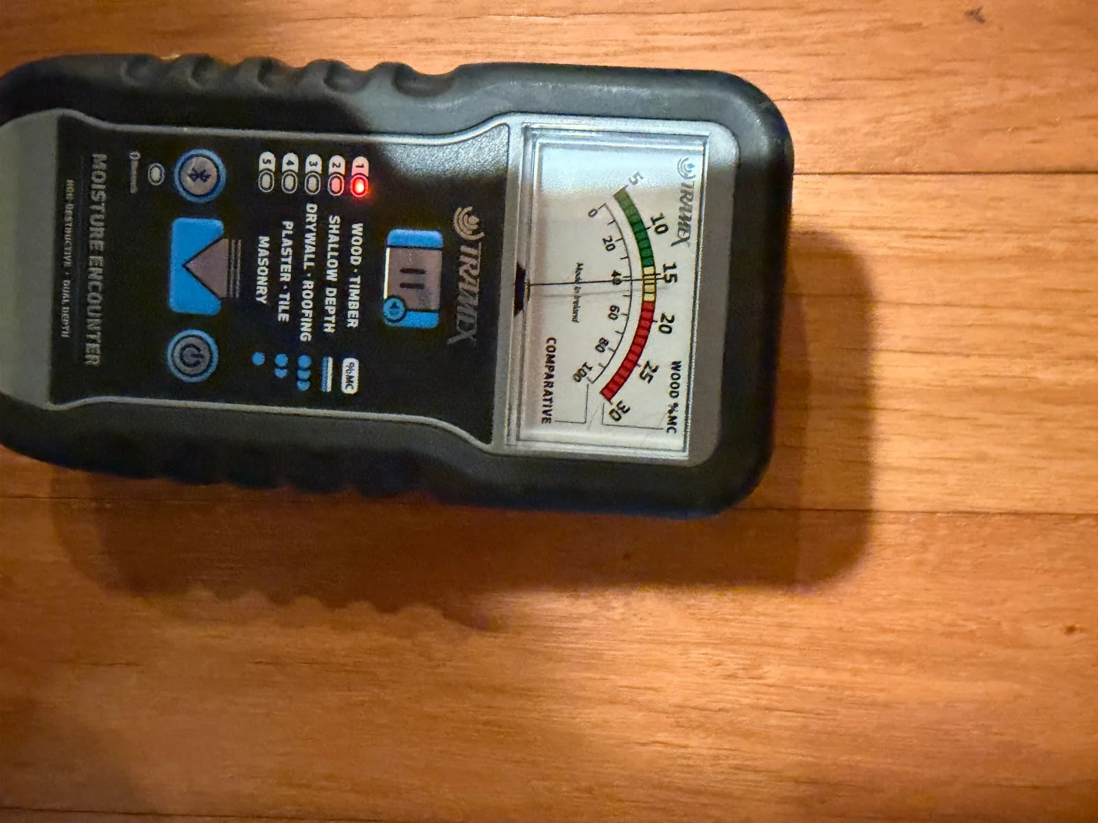 Pin-less moisture meter laid on a hardwood floor showing an elevated reading over a hidden leak area