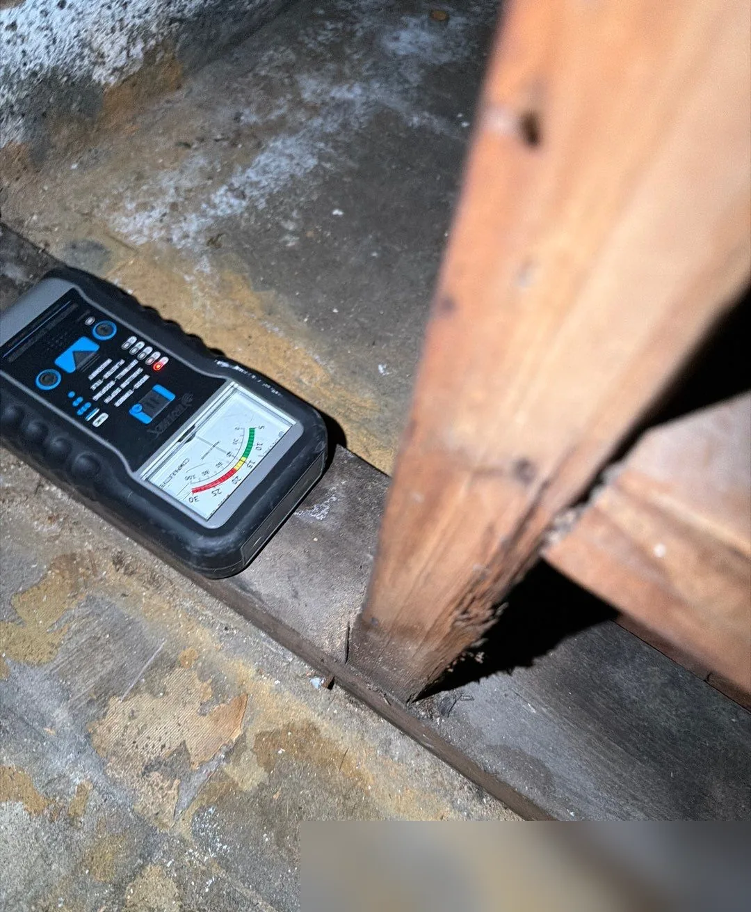 Moisture meter resting on a wood sill plate next to a stud to check for water that wicked into the framing