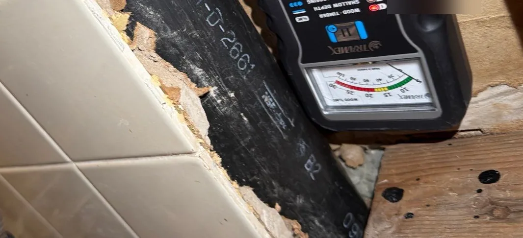 Tile tub surround cut open to the framing, with a pin-less moisture meter on the exposed wood during a hidden shower leak inspection