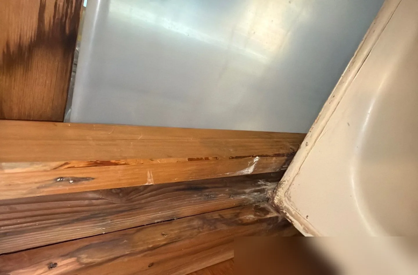 Water-stained and rotting wood framing exposed behind the edge of a bathtub after a slow hidden leak